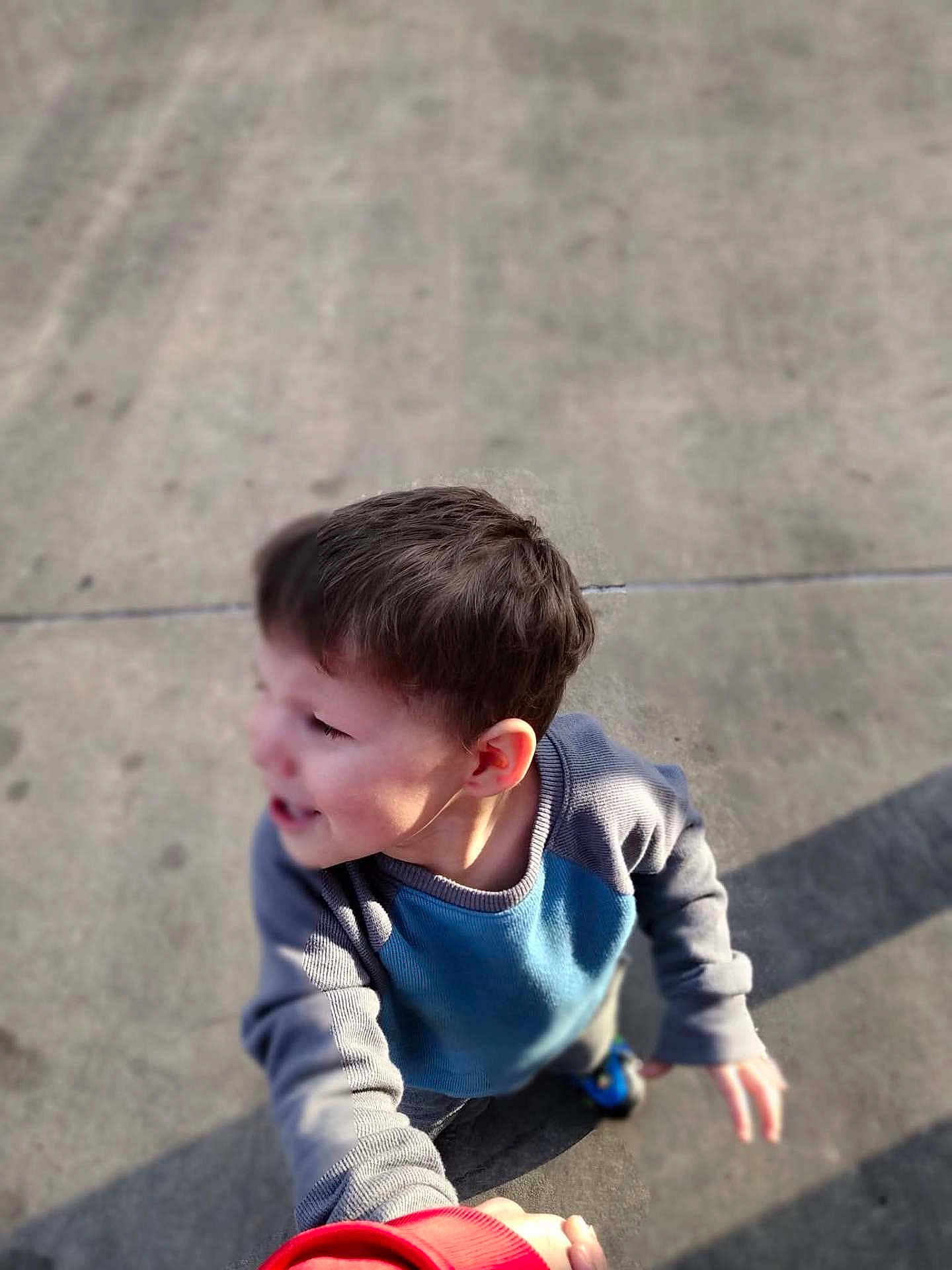 Jonathan is registered to the contest to win money with this photo: child, boy, sweater, hand_holding, outdoor, concrete, shadow, casual_clothing, short_hair, happy, young, person, daylight, looking_away, playing, standing, fun, interaction, childhood, casual
