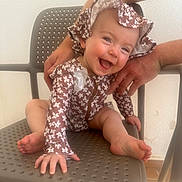 Hattie is registered to the contest to win money with this photo: baby, child, smiling, hat, floral_pattern, clothing, sitting, chair, hand, support, happy, face, foot, indoor, person, cute, infant, skin, expression, joy