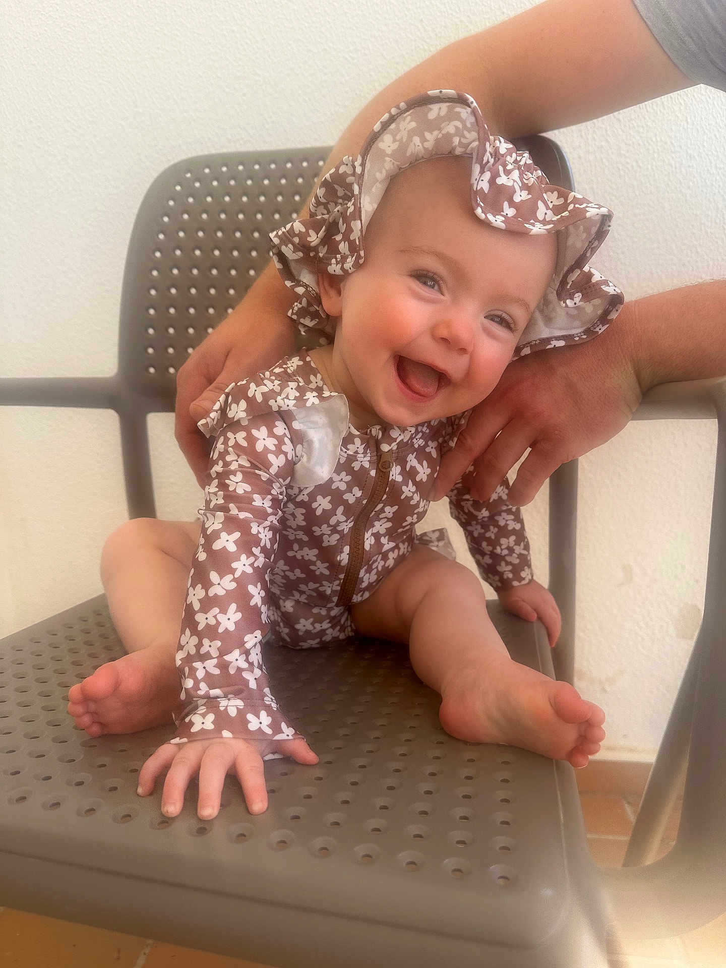 Hattie is registered to the contest to win money with this photo: baby, child, smiling, hat, floral_pattern, clothing, sitting, chair, hand, support, happy, face, foot, indoor, person, cute, infant, skin, expression, joy