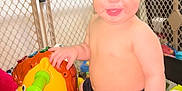 Miles is registered to the contest to win money with this photo: toddler, child, smiling, toy, horse, indoor, play_area, baby, shorts, shirtless, fence, plastic_toy, colorful, cute, happy, person, playtime, young_child, home, fun