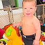 baby, child, colorful, cute, fence, fun, happy, home, horse, indoor, person, plastic_toy, play_area, playtime, shirtless, shorts, smiling, toddler, toy, young_child
