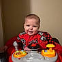 Miles is registered to the contest to win money with this photo: toddler, child, toy_car, steering_wheel, red_clothing, indoor, play, happy, smiling, racing_theme, buttons, plastic_toy, baby, seat, young_child, face, person, wall, playtime, fun