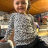 child, toddler, smiling, leopard_print, shirt, curly_hair, indoor, living_room, furniture, couch, decorations, portrait, happy, person, casual_clothing, seated, young_child, cute, home, cozy