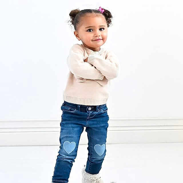 Tre'Me is registered to the contest to win money with this photo: child, girl, standing, crossed_arms, jeans, heart_patch, boots, smile, cute, portrait, fashion, studio, white_background, hair_buns, casual_clothing, confident, photography, young, happy, toddler