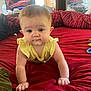 baby, child, crawling, yellow_clothing, red_bedspread, bedroom, indoor, television, guitar, furniture, window, water_bottle, toy, curious, face, person, skin, head, arm, hand
