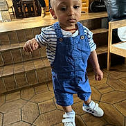 Diego a rejoint le concours — aidez-le/la à gagner de superbes lots ! toddler, child, blue_overalls, white_sneakers, striped_shirt, indoor, tile_floor, stairs, wooden_furniture, person_walking, necklace, baby, footwear, floor, person, home, casual_clothing, young_child, walking, expression