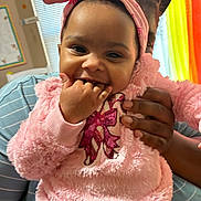 Maverick joined the competition — help win amazing prizes! baby, child, pink_clothing, headband, smiling, hand, adult_hand, indoor, window, curtains, striped_shirt, person, happy, cute, toddler, playful, seated, face, fingers_in_mouth, cozy