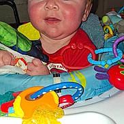 Greyson is registered to the contest to win money with this photo: baby, child, toys, highchair, colorful, indoor, smile, face, red_clothing, plastic_toys, teether, playtime, cute, infant, young_child, expression, human, portrait, closeup, seat