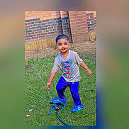 Kabir is registered to the contest to win money with this photo: child, toddler, sprinkler, water, grass, garden, brick_wall, blue_clothing, wet_shirt, smiling, outdoor, play, summer, greenery, fence, toy, happy, barefoot, person, lawn