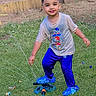 child, boy, outdoor, grass, sprinkler, water, playing, blue_pants, blue_shoes, tshirt, smiling, garden, backyard, brick_wall, water_spray, fun, happy, summer, foot_on_sprinkler, casual_clothing