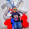 balloons, birthday, blue_balloons, carpet, celebration, child, happy, indoor, jeans, number_balloons, party, red_balloons, shirt, smiling, socks, standing, sunglasses, superhero, toddler, wall