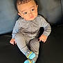 Isaiah is registered to the contest to win money with this photo: toddler, child, onesie, socks, minion, couch, leather, black, indoor, portrait, sitting, curious, expression, face, hair, clothing, person, baby, comfortable, casual