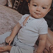 Isaiah is registered to the contest to win money with this photo: toddler, child, baby, carpet, indoor, white_shirt, pants, sitting, curly_hair, hand, foot, furniture, cozy, home, person, portrait, floor, expression, cute, young