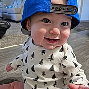 Elijah joined the competition — help win amazing prizes! baby, child, blue_cap, smile, onesie, tree_pattern, indoor, floor, living_room, cute, happy, face, person, infant, sitting, clothing, headwear, cheerful, portrait, young