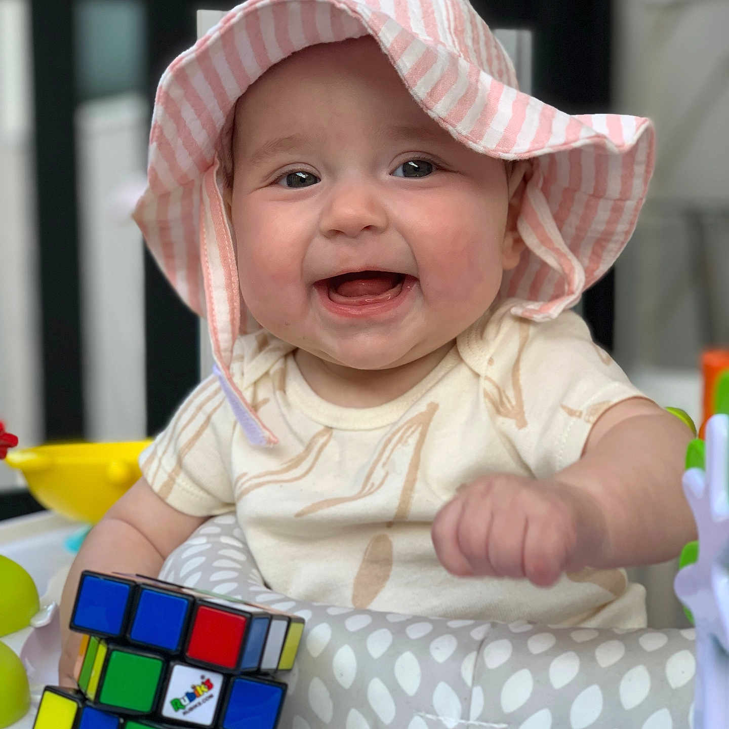 Paisley is registered to the contest to win money with this photo: baby, bodypart, bonnet, cap, clothing, dress, face, finger, hand, happy, hat, head, laughing, person, photography, portrait, sitting, smile, sunhat, toy