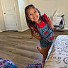 child, girl, smiling, happy, denim_overalls, red_shirt, long_hair, indoor, wood_floor, living_room, window, door, blanket, couch, playful, pose, sock, home, cheerful, person