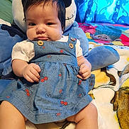Hazel is registered to the contest to win money with this photo: baby, child, blue_dress, plush_toy, blanket, indoor, cute, sitting, face, hands, legs, button, pattern, fabric, toy, bedroom, curtain, colorful, soft, comfort