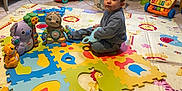 Gabriel a rejoint le concours — aidez-le/la à gagner de superbes lots ! toddler, child, toy, playmat, indoor, colorful, puzzle_mat, floor, plastic_toys, baby, child_playing, furniture, radiator, box, floor_tiling, smiling, cute, seated, blue_clothing, playroom