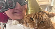 Eddie is registered to the contest to win money with this photo: cat, orange_cat, fluffy, long_hair, pet, party_hat, new_year, celebration, human, person, portrait, close_up, indoors, kitchen, cabinets, glasses, costume, whiskers, green_eyes, festive