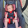 baby, bare_feet, blue_eyes, buckled, car_seat, child, deck, face, hands, harness, infant, outdoor, photograph, pink_blanket, polka_dots, portrait, red_outfit, sitting, vehicle_seat, wooden_deck
