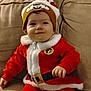Raine joined the competition — help win amazing prizes! baby, child, couch, cozy, cute, face, festive, fur_trim, happy, hat, holiday, indoors, infant, person, portrait, red_clothing, santa_outfit, sitting, smile, warm_clothing