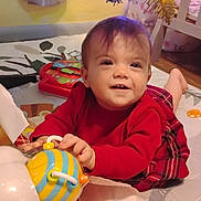 Raine is registered to the contest to win money with this photo: baby, child, toy, red_sweater, plaid_skirt, playmat, indoor, smiling, face, hand, floor, nursery, colorful, bee_toy, box, furniture, cute, happy, infant, person