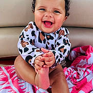 Lylah joined the competition — help win amazing prizes! baby, child, curly_hair, smiling, happy, towel, pink, patterned, clothing, foot, hand, face, sitting, indoors, cute, infant, skin, person, playful, joyful