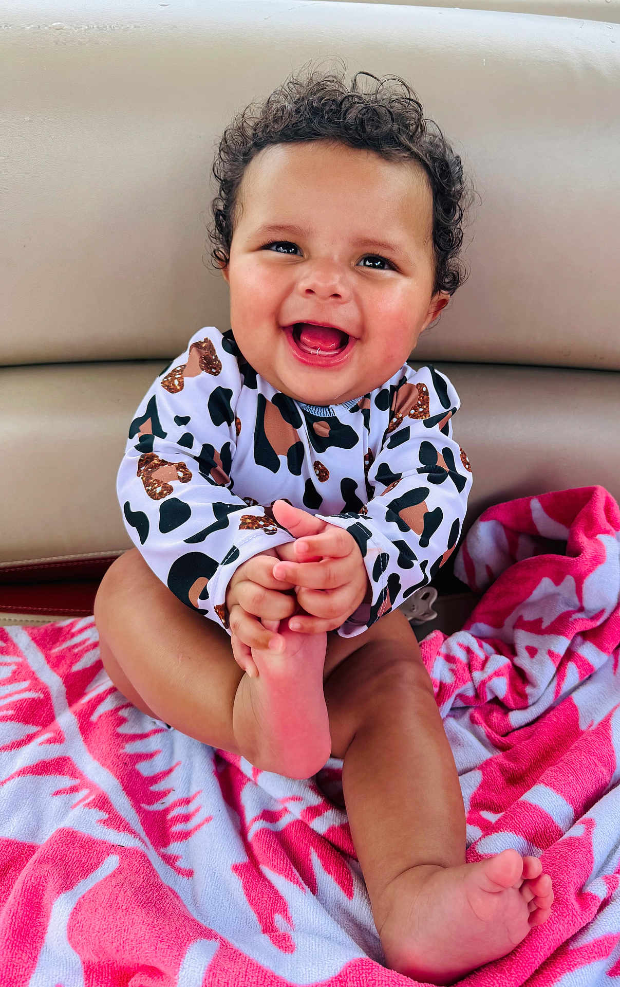 Lylah joined the competition — help win amazing prizes! baby, child, curly_hair, smiling, happy, towel, pink, patterned, clothing, foot, hand, face, sitting, indoors, cute, infant, skin, person, playful, joyful