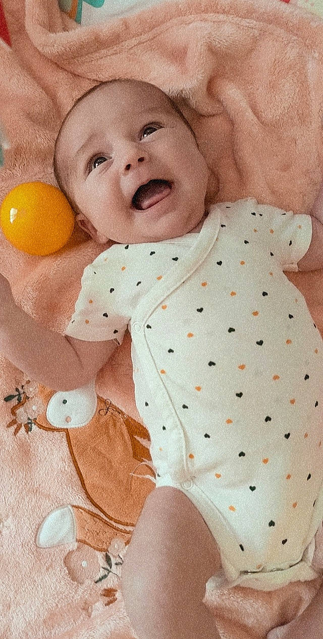 Luna a rejoint le concours — aidez-le/la à gagner de superbes lots ! baby, baby_products, baby_sleeping, baby_toddler_clothing, collar, comfort, face, happy, headwear, linens, orange, pattern, person, pink, product, skin, sleeve, smile, textile, thigh