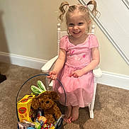 Emilena Joy joined the competition — help win amazing prizes! child, girl, pink_dress, pigtails, white_chair, basket, stuffed_animal, plush_dog, candy, easter_eggs, carpet, indoor, smiling, happy, toy, home, wall, staircase, footwear, person