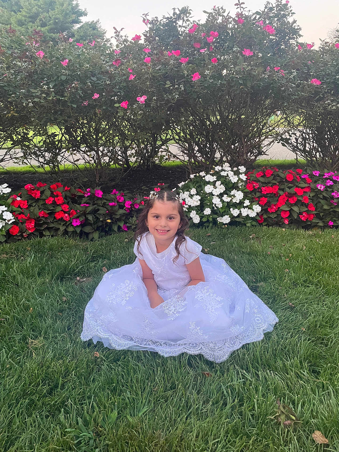 Valentina Rose is registered to the contest to win money with this photo: child, girl, white_dress, grass, flowers, bushes, smile, outdoor, nature, greenery, portrait, happy, young, pretty, colorful, garden, sitting, flower_bed, daylight, cute