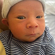 Luca is registered to the contest to win money with this photo: baby, newborn, infant, face, hat, striped_shirt, closeup, person, child, skin, eyes, expression, clothing, portrait, headwear, indoor, soft_light, cute, newborn_clothing, serious