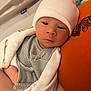 Luca is registered to the contest to win money with this photo: baby, newborn, infant, hat, blanket, striped_clothing, orange_cushion, resting, peaceful, indoor, person, face, headwear, wrapped, closeup, soft_texture, sleepy, cute, human, comfort