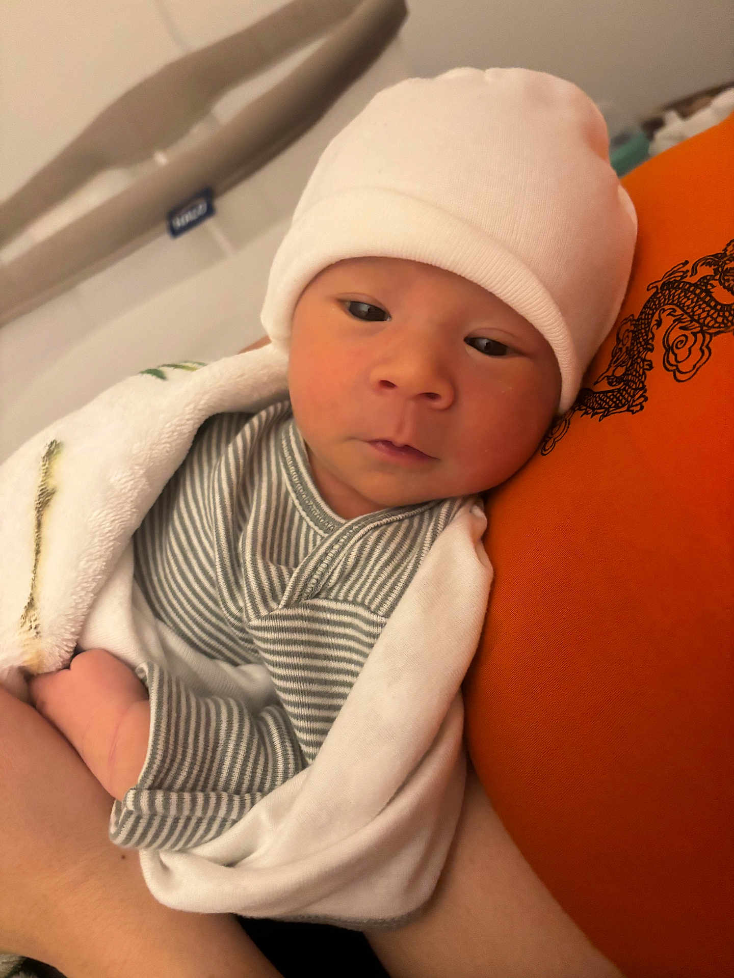 Luca is registered to the contest to win money with this photo: baby, newborn, infant, hat, blanket, striped_clothing, orange_cushion, resting, peaceful, indoor, person, face, headwear, wrapped, closeup, soft_texture, sleepy, cute, human, comfort