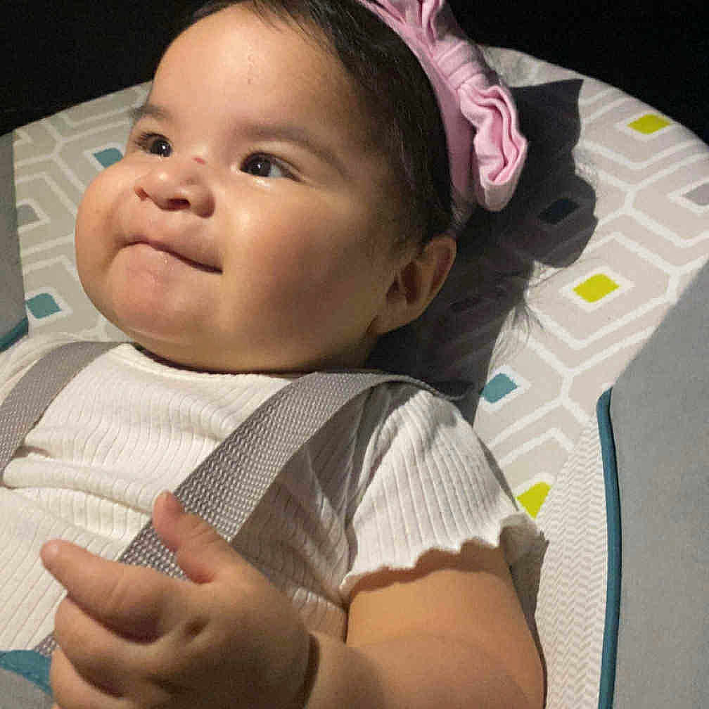 Heavenly Roze is registered to the contest to win money with this photo: baby, baby_girl, cheeks, child, closeup, curious, cute, expression, face, hand, headband, indoors, infant, pattern, pink_bow, portrait, seat, straps, white_shirt, young