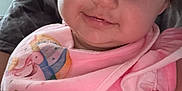 Mary joined the competition — help win amazing prizes! baby, child, infant, pink_clothing, bib, smile, face, eyes, person, indoor, cute, happy, young_child, skin, hair, sitting, holding, apparel, portrait, closeup