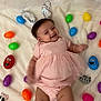 Mary joined the competition — help win amazing prizes! baby, child, pink_dress, bunny_ears, easter_eggs, colorful, smiling, happy, infant, toys, plastic_eggs, blanket, cute, playful, celebration, holiday, festive, lying_down, face, soft_texture