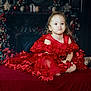 child, girl, red_dress, pout, sitting, holiday_decor, festive, portrait, cute, expression, indoor, decorations, christmas, celebration, smile, cute_face, young_child, fancy_dress, toddler, happy