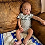 Creed is registered to the contest to win money with this photo: baby, infant, child, couch, blanket, onesie, striped_clothing, brown_couch, blue_and_white_blanket, relaxed, indoor, person, small_feet, armrest, seated, young_child, skin, head, face, expression