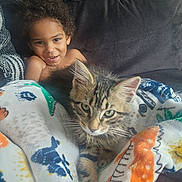 Ruger is registered to the contest to win money with this photo: child, kitten, cat, blanket, couch, indoor, curly_hair, smiling, young, pet, cozy, furniture, tabby, striped, relaxed, cute, comfort, home, domestic_animal, portrait