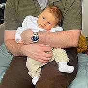 Louis participe au concours pour gagner de l'argent avec cette photo : adult, arm, baby, blue_eyes, clothing, comfort, couch, cushion, face, hand, holding, indoor, infant, pants, person, seated, skin, sock, watch, white_shirt