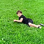 child, boy, grass, lawn, outdoor, greenery, casual_clothing, shorts, tshirt, sneakers, lying_down, curious_expression, nature, summer, recreation, play, park, daylight, young, person