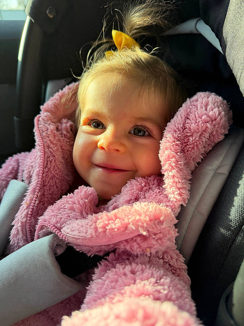 Elya a rejoint le concours — aidez-le/la à gagner de superbes lots ! baby, car_seat, child, closeup, cute, eyelashes, face, fluffy_clothing, hair, happy, indoors, person, pink_jacket, portrait, seatbelt, smile, toddler, warm_light, yellow_bow, young_child