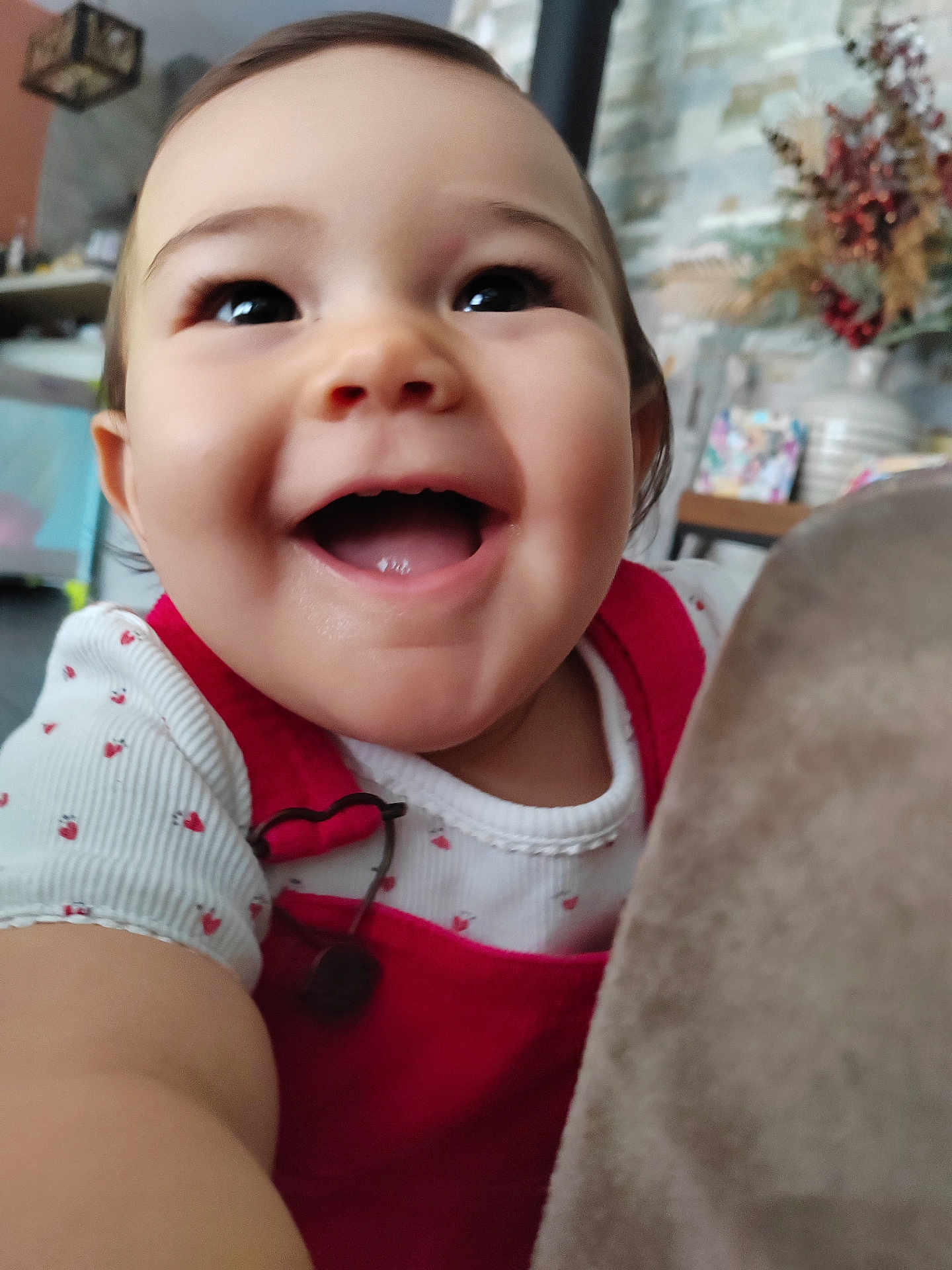 Emma participe au concours pour gagner de l'argent avec cette photo : baby, child, smiling, happy, face, closeup, indoor, red_clothing, white_shirt, heart_pattern, arm, cute, portrait, infant, person, home, decor, plant, background, joy