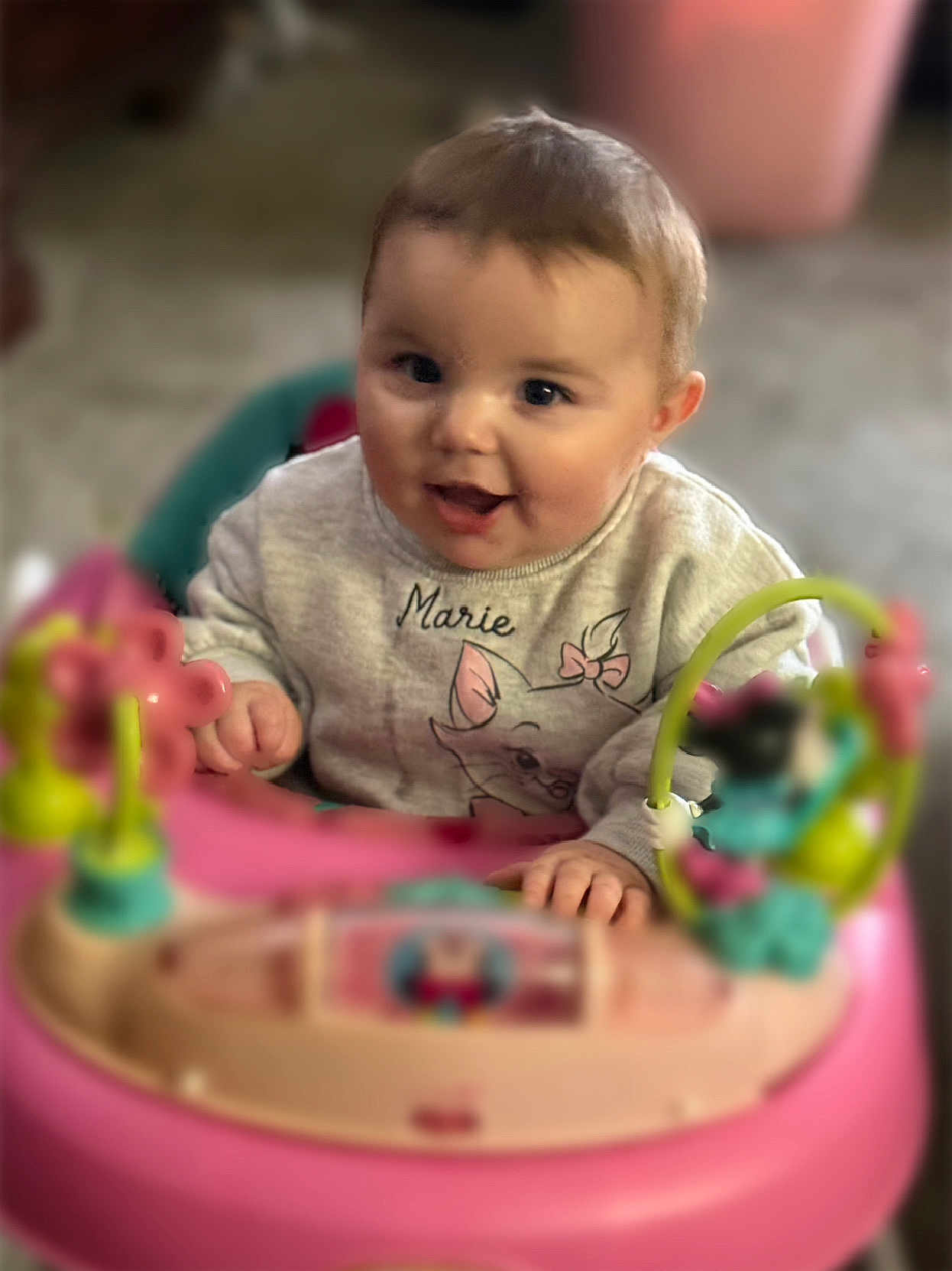 Zada is registered to the contest to win money with this photo: baby, infant, child, smiling, face, eyes, hands, cheeks, hair, sweater, name_on_shirt, toy, walker, pink_toy, play_center, indoors, floor, portrait, cute, playful
