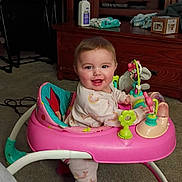 Zada is registered to the contest to win money with this photo: baby, baby_walker, pink_walker, smile, happy, living_room, television, wood_cabinet, toy, carpet, socks, clothing, face, portrait, playtime, wipes, bottle, furniture, cute, infant