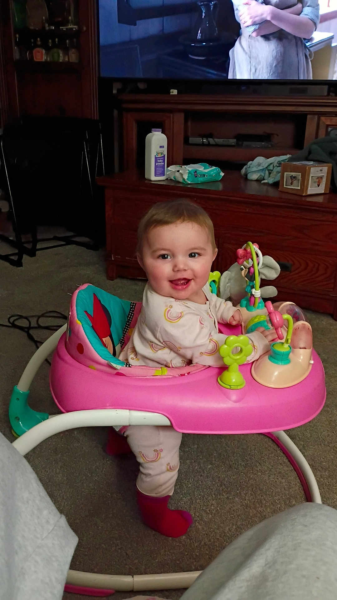 Zada is registered to the contest to win money with this photo: baby, baby_walker, pink_walker, smile, happy, living_room, television, wood_cabinet, toy, carpet, socks, clothing, face, portrait, playtime, wipes, bottle, furniture, cute, infant