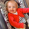 baby, child, infant, red_cardigan, striped_clothing, baby_seat, patterned_cushion, happy, smiling, blue_eyes, light_hair, indoors, cute, portrait, sitting, young_child, clothing, toddler, playful, cozy