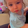 toddler, child, baby, blue_eyes, light_blue_shirt, dark_shorts, indoor, person, curious_expression, close_up, sitting, lap, hair, young_child, cute, face, hand, furniture, background, household_items