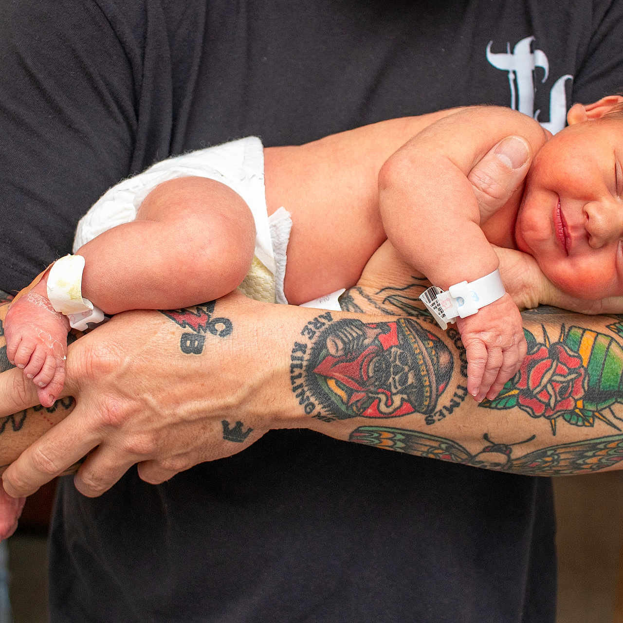 Sutton is registered to the contest to win money with this photo: baby, newborn, infant, tattoo, arm, diaper, sleeping, smiling, person, human, skin, hand, hospital_band, closeup, indoor, parent, holding, peaceful, cute, love